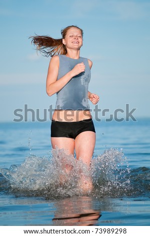 Beautiful young sport woman running in water on sunny summer day