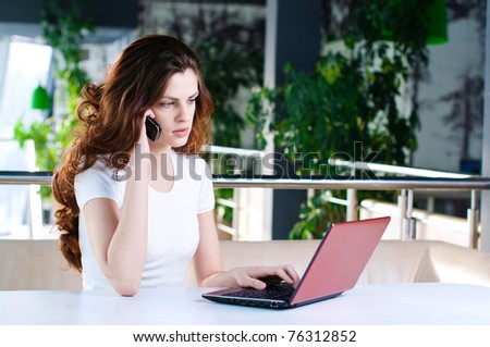 A young attractive business woman sitting in a cafe with a laptop and cell phone