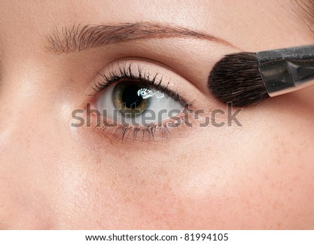 Beautiful young woman applying cosmetic paint brush - close-up portrait of eye shadow zone