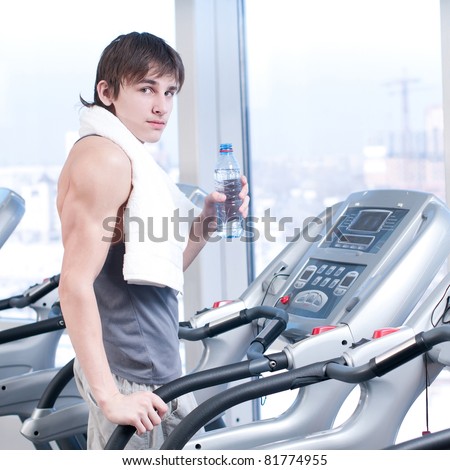 Young man at the gym exercising. Run on on a machine and drink water