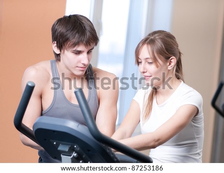 Woman and man train on machine in a gym assisted by personal instructor