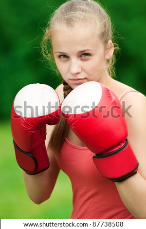 Beautiful young woman doing box exercise in red gloves at green park. Boxer