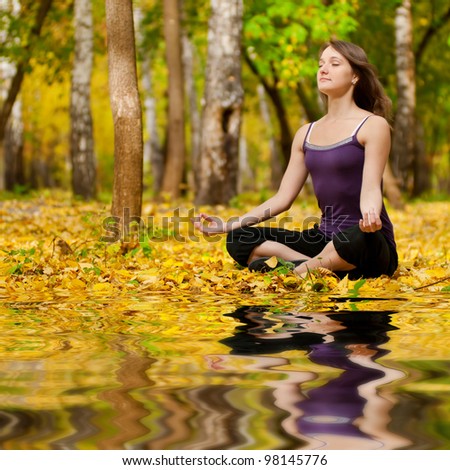 Young woman doing yoga exercises in the autumn city park lake. Fall with mirror in water