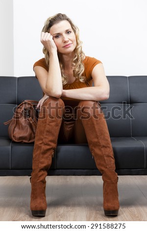 woman wearing brown clothes and boots with a handbag sitting on sofa