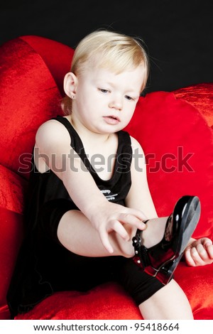 little girl with black shoes sitting on red armchair