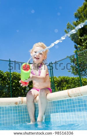 little girl with water sprayer by swimming pool