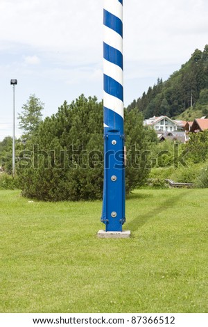 lower section of a tree trunk in blue and white painted stripes, a so-called May pole. It is a traditional sign typical for Bavaria to indicate the range of workers and craftsmen in the area