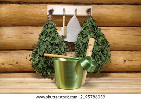 Green metal accessories and other traditional utensils for sauna are on a wooden bench and on a hanger on a log wall in the interior of a wooden bathhouse. ストックフォト © 
