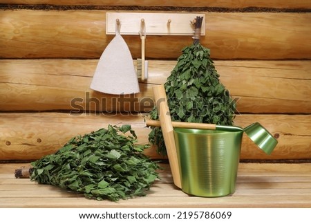 Green metal accessories and other traditional utensils for sauna are on a wooden bench and on a hanger on a log wall in the interior of a wooden bathhouse. ストックフォト © 