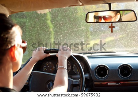 Young woman driving an old car. Selective focus on her hands and rear-view mirror.