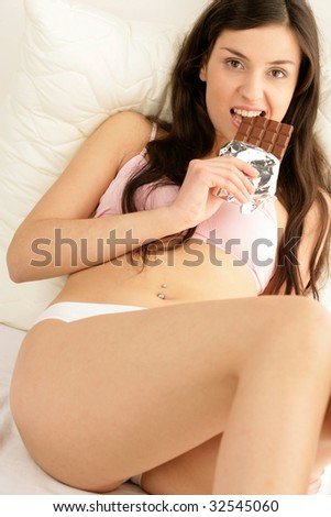 Woman eating chocolate bar lying down on bed