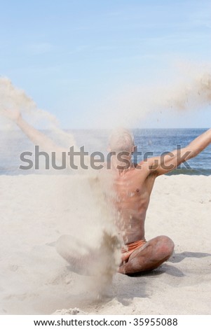 Handsome man sitting on the beach with crossed legs and throwing sand