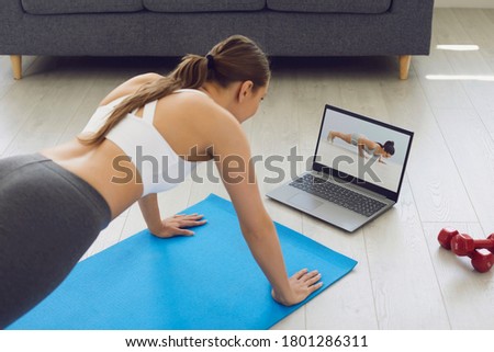 Fitness online. Young fit girl at home on the floor doing exercises, stretching warm-up and uses a video fitness lesson on the Internet.