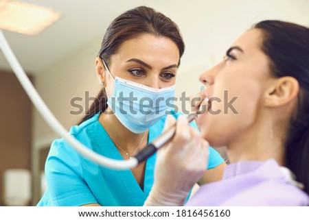 Dentist at work. Concentrated female specialist removing tooth stone from client's teeth using ultrasonic scaler. Young woman having professional painless teeth cleaning at modern dental office Stockfoto © 