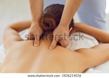 Men's hands do a therapeutic neck massage for a girl lying on a massage couch in a bright massage spa. Acupressure massage in spa centre. Body therapy for healthy lifestyle. Close up.