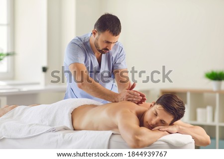 Relieving back muscle tension. Professional masseur massaging young man's back using Tapotement or chopping, tapping or hacking technique during Swedish massage therapy in spa salon or wellness center ストックフォト © 