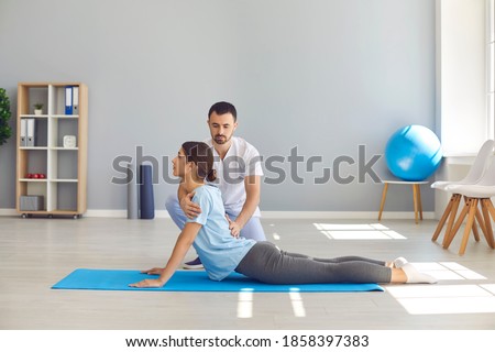 Side view of young female athlete doing back bending exercise during physiotherapy after sports injury. Health center specialist helping woman regain back flexibility after trauma Photo stock © 