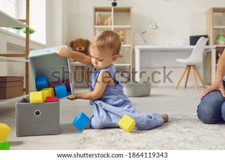 Little helper cleaning up and learning to be independent. Cute 2 year old child putting cubes back in their place after playing. Toddler boy putting toys away sitting on warm floor in nursery room Foto d'archivio © 