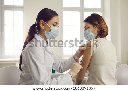 Professional doctor or nurse giving flu or COVID-19 injection to patient. Woman in medical face mask getting antiviral vaccine at hospital or health center during vaccination and immunization campaign