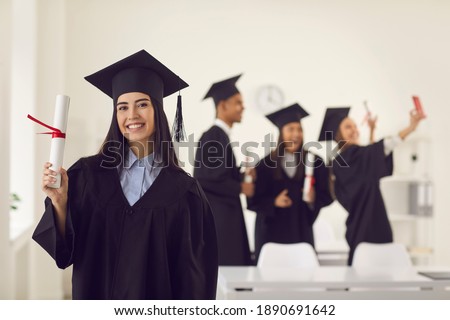 Female graduate dressed in a bachelor's gown shows the camera a diploma in her hands while standing in the classroom against the background of classmates who is taking a selfie. Education concept. Zdjęcia stock © 