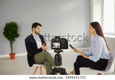 Digital video camera on tripod recording interview with a person in television studio. TV show host talking to celebrity. Journalist or reporter asking famous businessman questions. Blurred background
