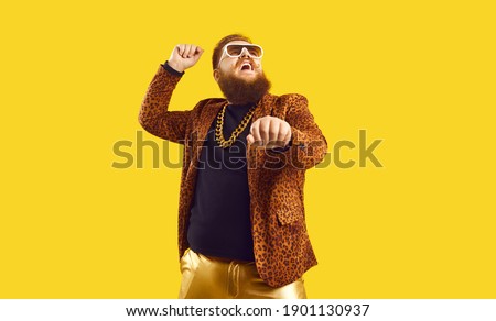 Happy funny plump young man singing songs and dancing gangnam style at a party. Funky redhead chubby guy having fun and doing rope dance move like cowboy with lasso isolated on amber color background