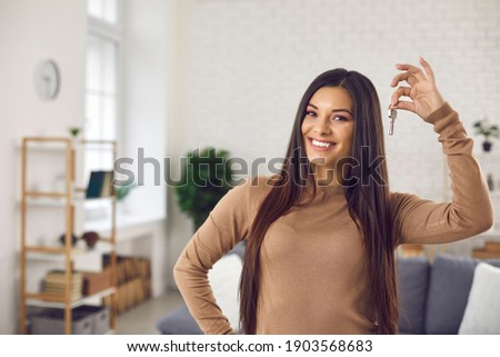 Happy woman holding keys to new home, looking at camera and smiling. Portrait of first time buyer, house owner, apartment renter, flat tenant or landlady. Moving day and buying own property concept