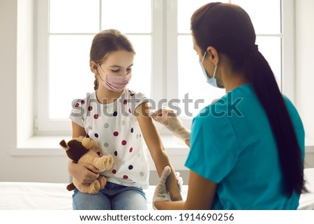 Vaccination concept. Little kid in medical face mask getting Covid-19 or flu vaccine at clinic. Woman who works as nurse or doctor at hospital disinfects skin on child's arm before giving injection
