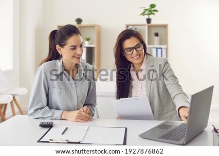Happy single young business woman consulting bank manager, financial advisor or loan broker. Smiling estate agent meeting client at office, talking, showing and offering house design options on laptop