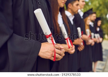 Close-up of young university graduates hands holding diplomas after university graduating outdoors, selective focus. Graduating from university or college concept