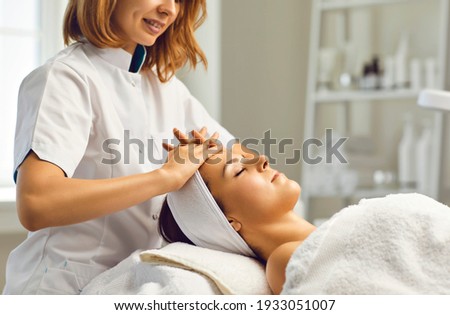 Cosmetologist or dermatologist making facial beauty massage treatment for relaxed young woman face with fingers movements in beauty spa salon. Facial treatment, massage, skincare, cosmetology concept