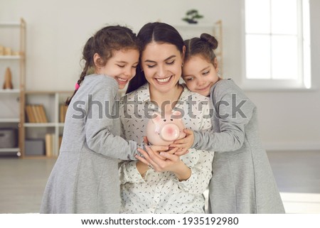 Little kids learning to value money. Happy young single mother and two cute daughters holding piggy bank and smiling. Saving up for children's education, family finance, and budget management concept