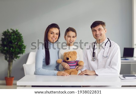 Smiling mother, child and family practitioner looking at camera sitting at table at doctor's office all together. Portrait of happy mom, healthy kid and friendly pediatrician in modern health center 商業照片 © 
