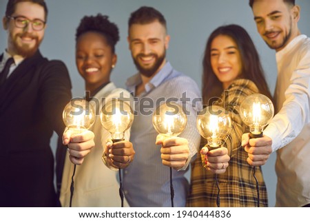 Happy creative team holding glowing lit lightbulbs. Diverse collaboration group of intelligent young multicultural business people with shining light bulbs presenting and sharing effective useful idea