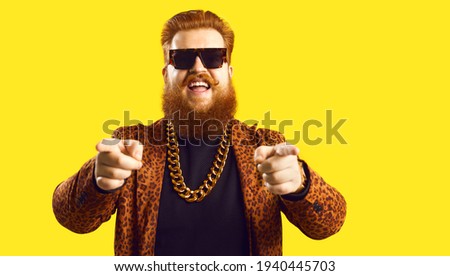 Happy guy in gold necklace and leopard suit pointing fingers at camera isolated on color background. Famous fashion designer, rich showbiz producer, casting director, funny celebrity says I choose you