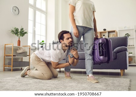 Young married couple breaking up. Angry woman leaving home with packed suitcase. Clingy desperate husband on floor holding wife's leg begging his love to stay. Relationship breakup and divorce concept Foto d'archivio © 