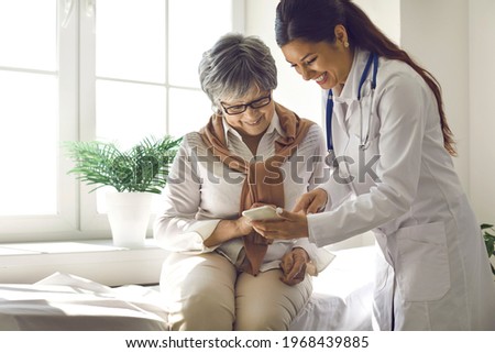 Caring doctor teaches female patient to use mobile healthcare app. Retired lady sitting in hospital exam room looking at cell screen learning to download health tracker for senior citizens. Copy space