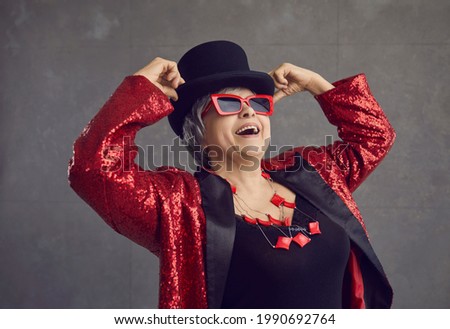 Portrait of party queen, actress, fashion model and cool grandma in crazy outfit looking up with admiration on gray background. Elegant senior woman having fun, enjoying leisure and positive emotions