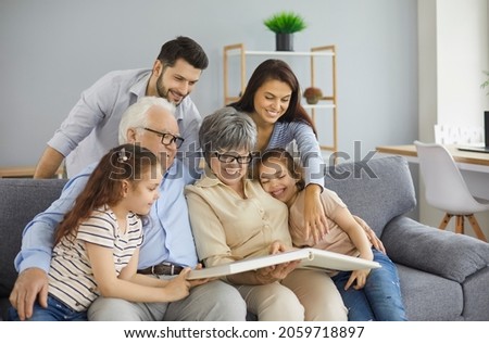 Happy big family grandparents with twin granddaughters and their parents browse the family photo album and share happy memories. Family gathered together in the living room. Family connection concept. Foto stock © 