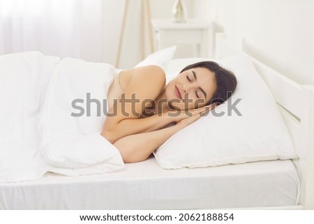 Tranquil Caucasian woman sleeping alone on side with hands under cheek. Pretty brunette european lady enjoying good night's rest in comfortable bed on soft pillow and natural organic cotton bedclothes Stock fotó © 