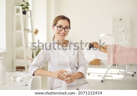 Portrait of happy young female dermatologist, skin therapist, beautician and skincare professional at work. Beautiful woman in clean white coat uniform and glasses sitting in her office and smiling Foto d'archivio © 