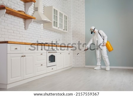 Exterminator fighting rodents, termites or cockroaches in the house. Pest control guy in a mask and protective white suit spraying poison from a sprayer bottle all over kitchen cupboards and cabinets Zdjęcia stock © 