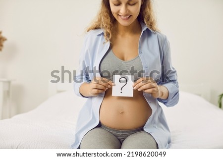 Happy mom-to-be thinking of name for her baby. Smiling pregnant lady trying to guess gender of unborn baby. Beautiful young woman sitting on bed with question mark card in hands. Gender reveal concept Stockfoto © 