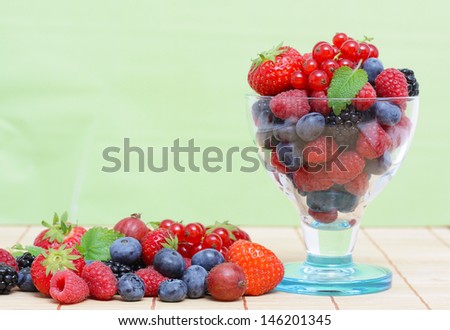 Fresh forest berries in a glass on green background
