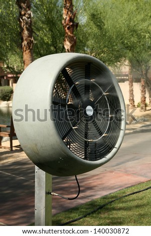 a water mister fan blows cool water into the air to cool down the area outside on a hot summer day
