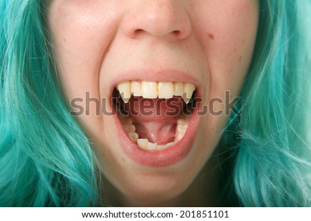 A young woman with blue hair wears black contact lenses and her Vampire Fangs. Isolated on white with room for your text
