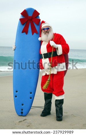 Santa Claus stands on the beach by the Ocean holding a Blue Surfboard with a Large Red Bow on it as a Christmas Gift to some lucky Boy or Girl. Santa Claus is one cool cat and love to give things out