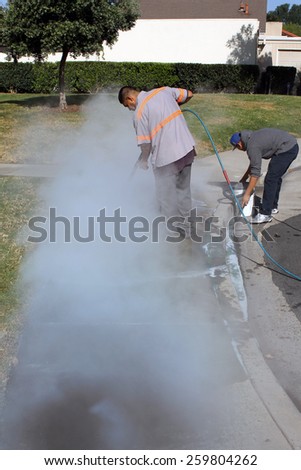Lake Forest California - March 010,.2015 : Workers use hot water steam pressure washers and paint remover to eliminate graffiti spray painted on to a city sidewalk.