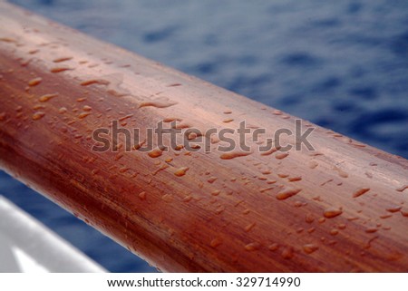 Wooden hand rail on an ocean liner with rain drops with the Caribbean ocean in the background.