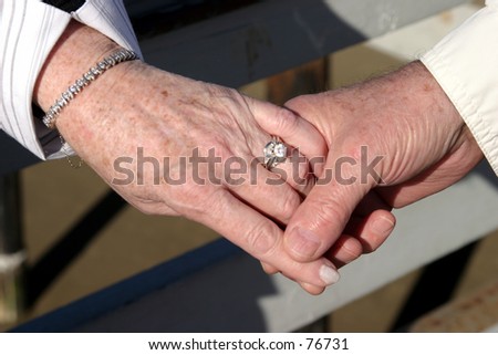 An older couple holds hands showing a wedding ring a brcelet and that love is in the air